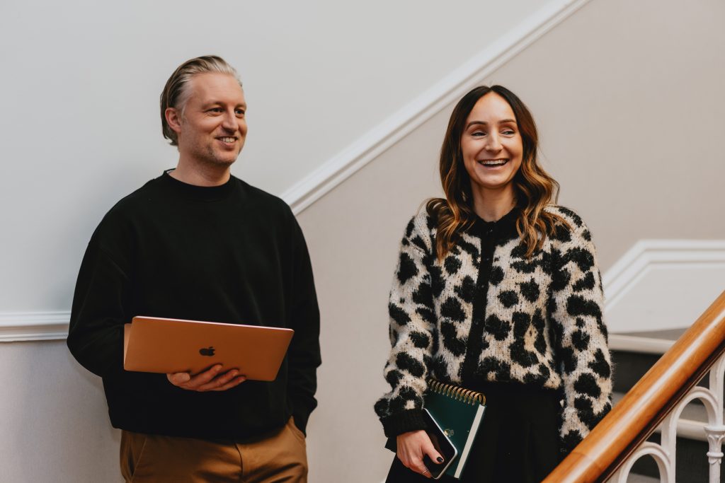 Two marketing professionals stood laughing with eachother in an office building.