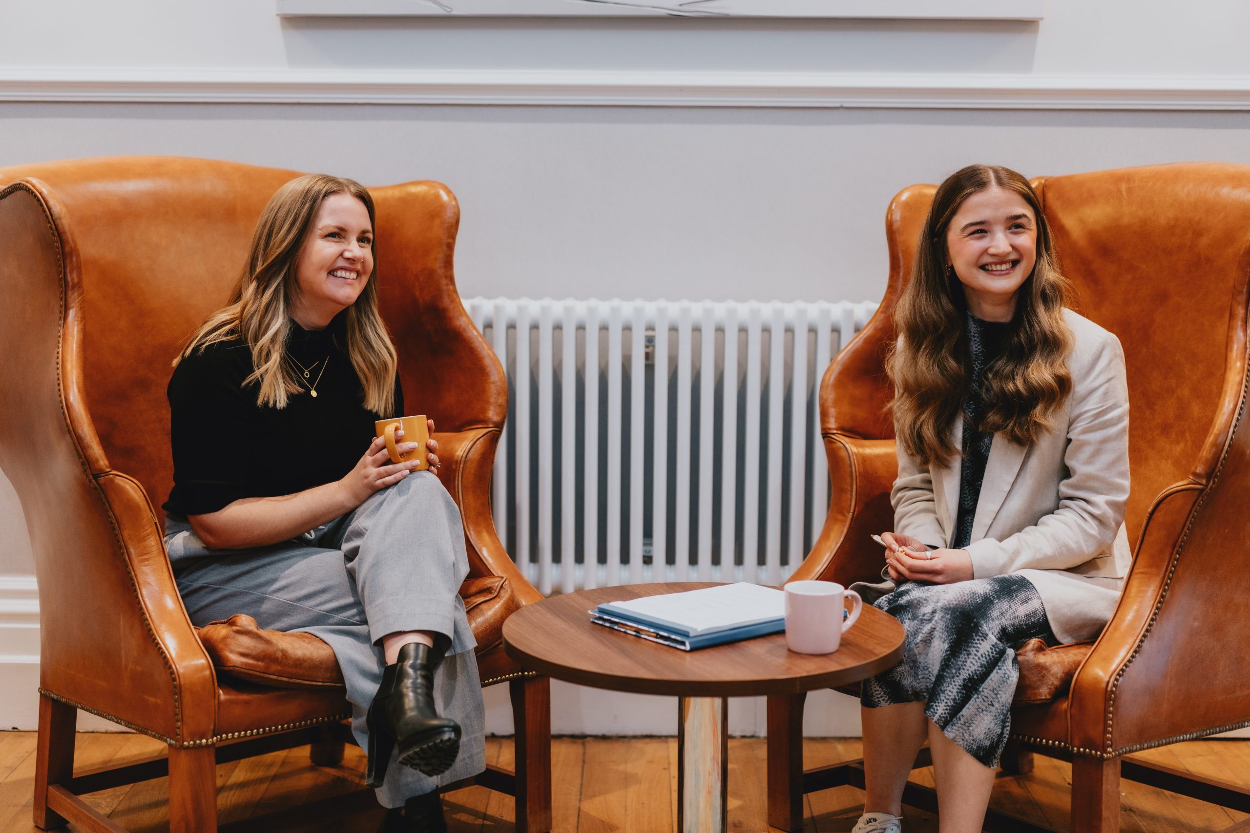 Employer and employee sat in big chairs, smiling at someone off camera